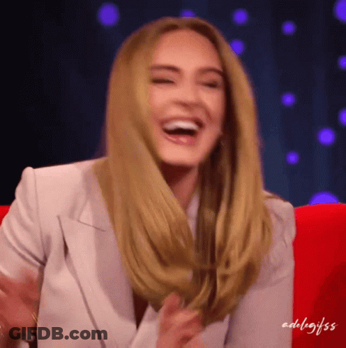 A Woman In A White Jacket Is Laughing While Sitting In A Chair GIF