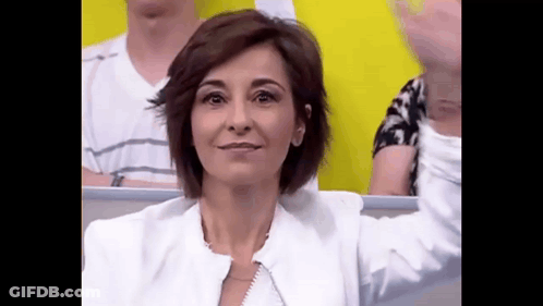 A Woman In A White Jacket Is Sitting In A Stadium With Her Arms Outstretched . GIF