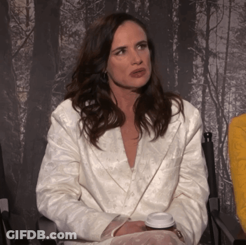 A Woman In A White Jacket Sits In A Chair With A Cup Of Coffee In Her Hand GIF