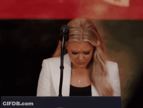 A Woman In A White Jacket Stands At A Podium With Her Eyes Closed GIF