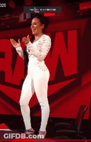 A Woman In A White Jumpsuit Is Clapping Her Hands In Front Of A Large Red N. GIF