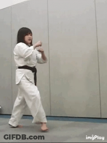 A Woman In A White Karate Uniform Is Kicking A Ball . GIF
