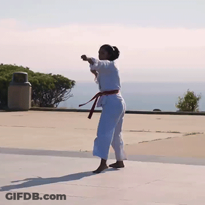 A Woman In A White Karate Uniform With A Red Belt Is Doing A Trick GIF