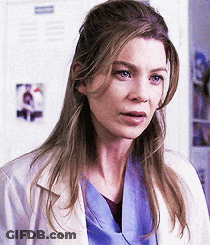 A Woman In A White Lab Coat And Blue Scrubs Stands In Front Of A Locker GIF