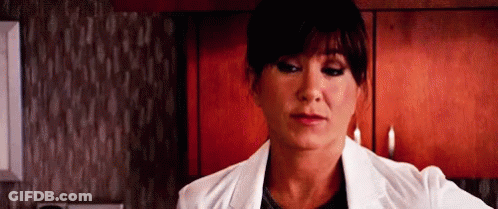 A Woman In A White Lab Coat Is Standing In A Kitchen Looking At The Camera . GIF