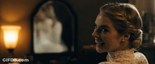 A Woman In A White Lace Dress Is Smiling In Front Of A Mirror GIF