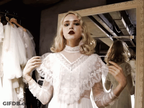 A Woman In A White Lace Dress Looks At Herself In A Mirror GIF