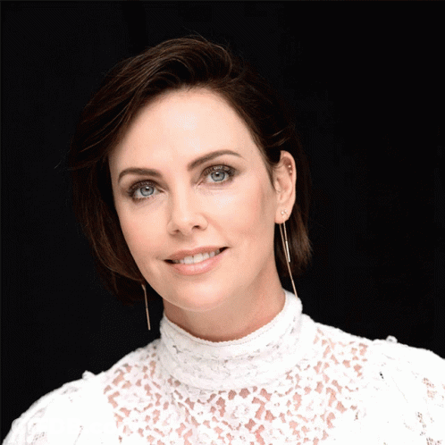 A Woman In A White Lace Top Has Her Hand On Her Chin GIF