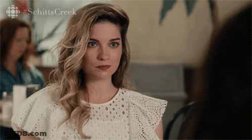A Woman In A White Lace Top With #Schitts Creek On The Bottom GIF