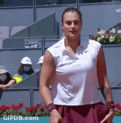 A Woman In A White Nike Shirt Is Holding A Tennis Racquet On A Tennis Court GIF