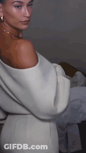 A Woman In A White Off The Shoulder Dress And Earrings GIF