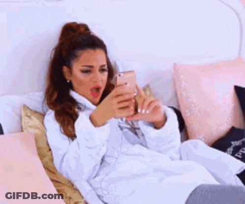 A Woman In A White Robe Is Laying On A Bed With Her Hands On Her Stomach . GIF