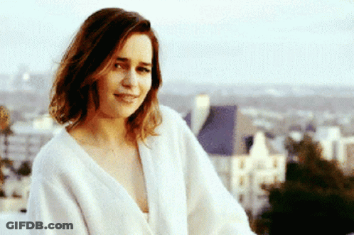 A Woman In A White Robe Is Smiling In Front Of A City GIF