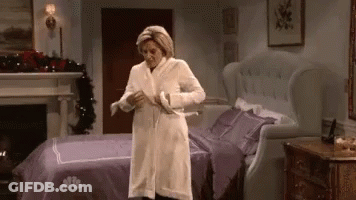 Woman In White Robe Standing Next To Bed GIF