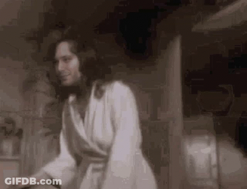 A Woman In A White Robe Is Standing In A Room . GIF