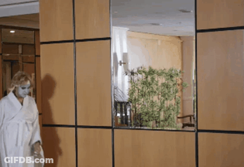 A Woman In A White Robe Is Standing In Front Of A Wooden Wall GIF