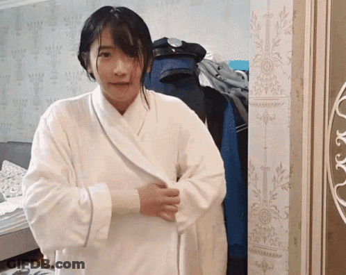 A Woman In A White Robe Stands In Front Of A Wall GIF