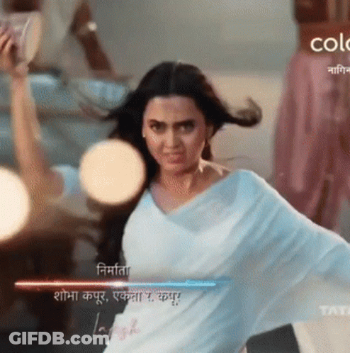 A Woman In A White Saree Is Dancing In Front Of A Sign That Says Color GIF