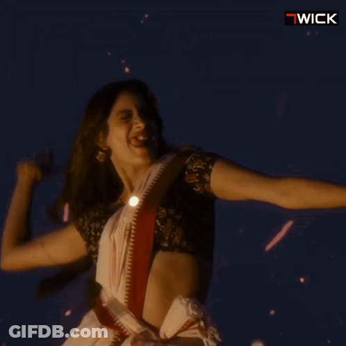 A Woman In A White Saree Is Dancing In Front Of A Sign That Says " Wick " GIF