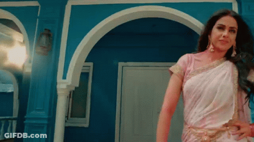 A Woman In A White Saree Stands In Front Of A Blue Wall GIF