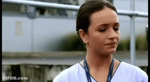A Woman In A White Scrub Top With A Lanyard Around Her Neck Is Crying . GIF
