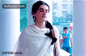 A Woman In A White Shawl Is Standing In A Hallway With Her Eyes Closed . GIF