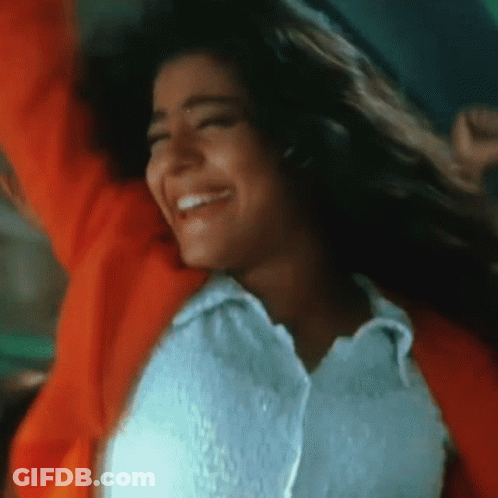 A Woman In A White Shirt And An Orange Jacket Is Smiling With Her Arms In The Air GIF