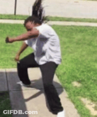 A Woman In A White Shirt And Black Pants Stands On A Sidewalk GIF