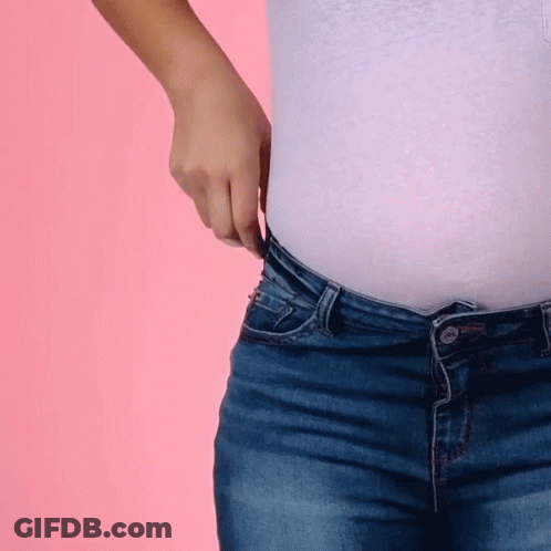 A Woman In A White Shirt And Blue Jeans Is Adjusting Her Waistband GIF