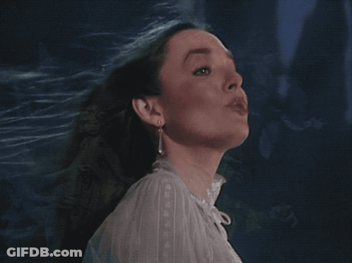 A Woman In A White Shirt And Earrings Looks Up GIF