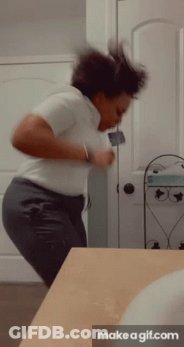 A Woman In A White Shirt And Gray Pants Is Dancing In Front Of A Bathroom Mirror . GIF