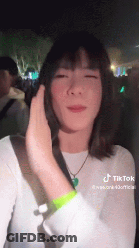 A Woman In A White Shirt And Green Wristband Is Standing In Front Of A Crowd . GIF