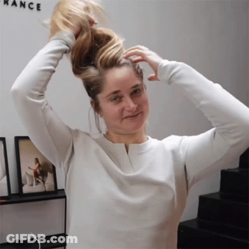 A Woman In A White Shirt Holds Her Hair In A Ponytail In Front Of A Wall That Says Rance GIF