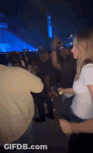 A Woman In A White Shirt Is Dancing In A Crowd Of People At A Concert . GIF