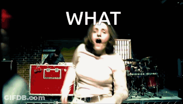 A Woman In A White Shirt Is Dancing In Front Of A Drum Set With The Word What Above Her GIF