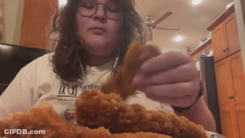 A Woman In A White Shirt Is Eating Fried Chicken . GIF