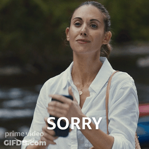 A Woman In A White Shirt Is Holding A Cell Phone With The Word Sorry Above Her GIF