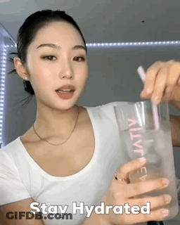 A Woman In A White Shirt Is Holding A Glass With A Pink Straw And The Words Stay Hydrated GIF
