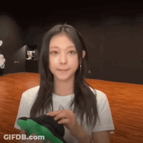 A Woman In A White Shirt Is Holding A Green Item In Her Hands GIF