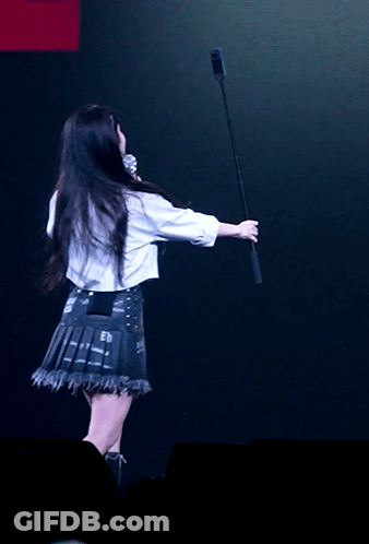 A Woman In A White Shirt Is Holding A Microphone In Her Hand GIF