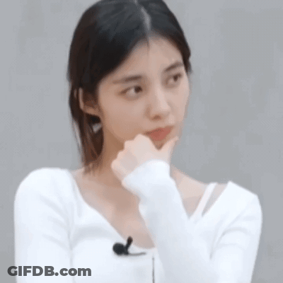A Woman In A White Shirt Is Holding Her Hand To Her Chin And Making A Funny Face . GIF