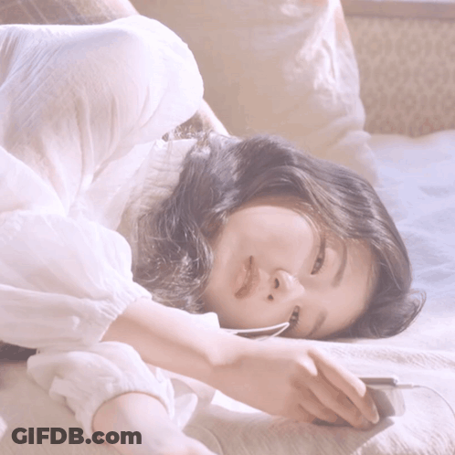 A Woman In A White Shirt Is Laying Down On A Bed GIF