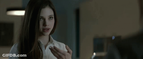 A Woman In A White Shirt Is Looking At A Man In A Dark Room . GIF