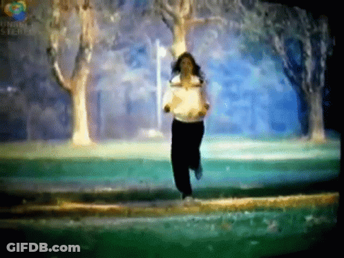 A Woman In A White Shirt Is Running In A Park With Trees In The Background .. GIF