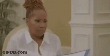 A Woman In A White Shirt Is Sitting At A Table Holding A Piece Of Paper In Her Hand . GIF