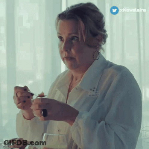 A Woman In A White Shirt Is Sitting At A Table With A Spoon In Her Hand And A Twitter Icon Above Her GIF