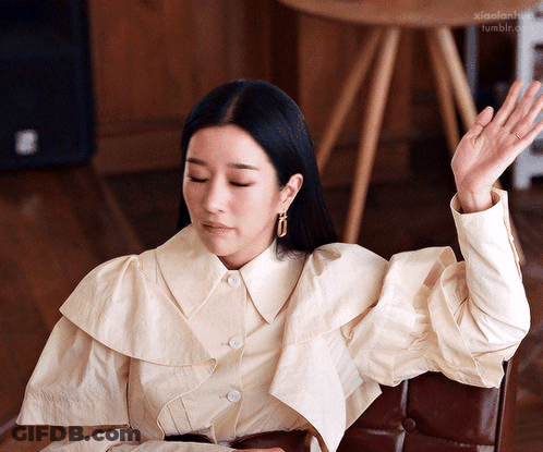 A Woman In A White Shirt Is Sitting In A Chair With Her Hand Up In The Air GIF
