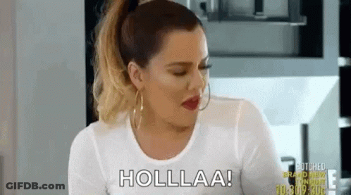 A Woman In A White Shirt Is Sitting In A Kitchen Talking To Someone . GIF