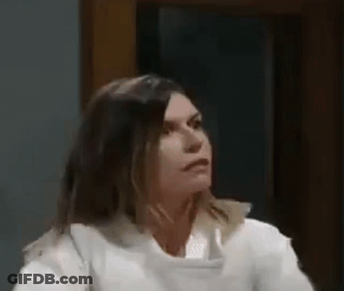 A Woman In A White Shirt Is Sitting In Front Of A Window And Looking At The Camera . GIF