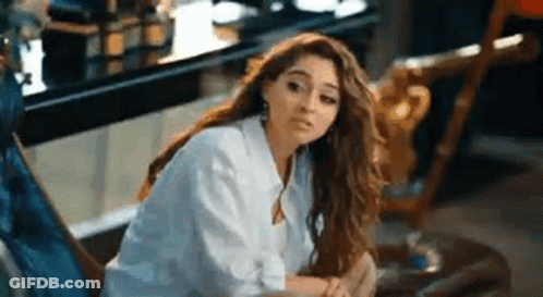 A Woman In A White Shirt Is Sitting On A Chair In A Room . GIF